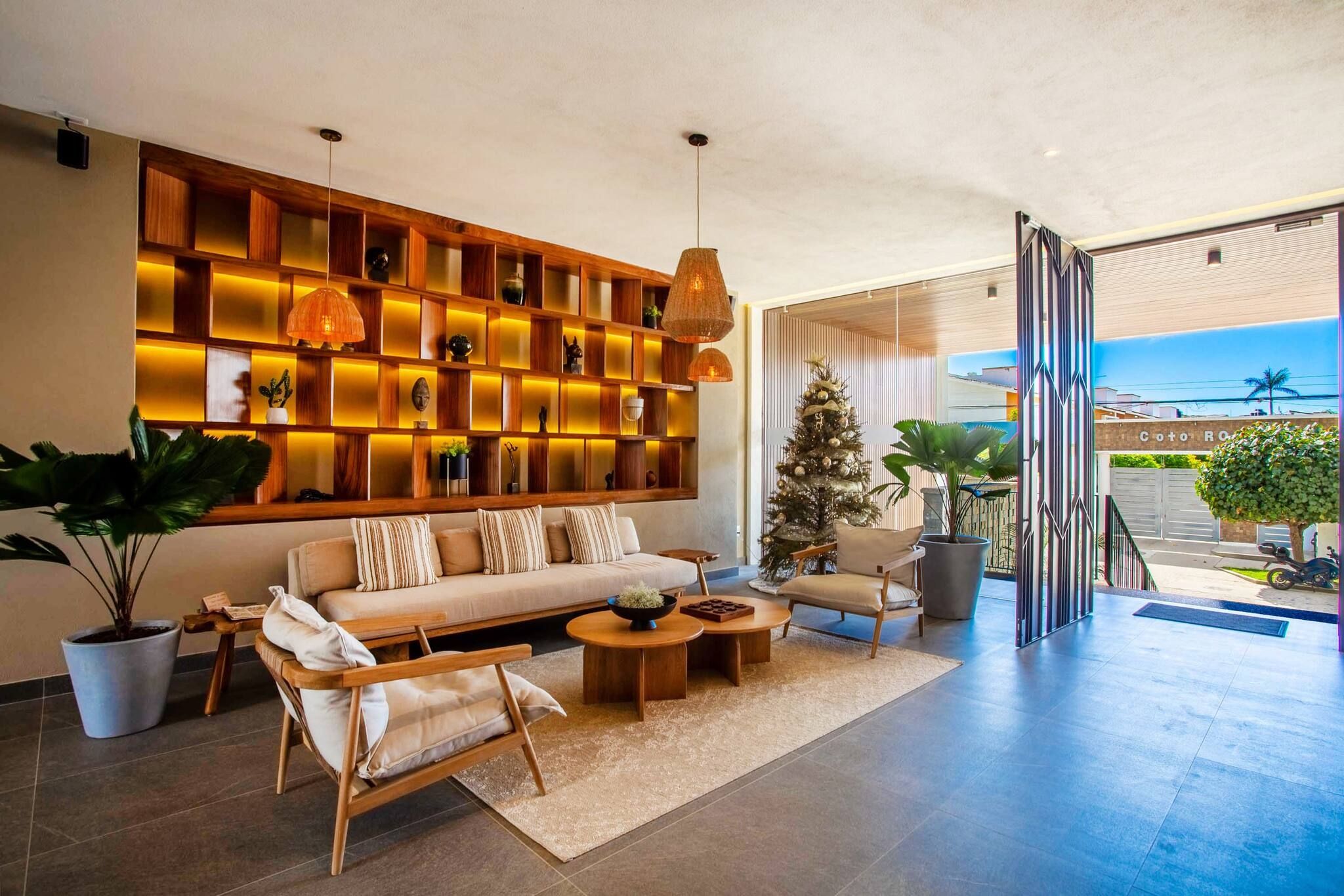 A modern living room with a sofa, coffee table, and side chairs. A large wooden shelf with illuminated panels is against the wall.
