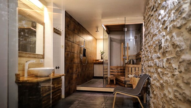 A modern bathroom with a large sink, wooden cabinets, a shower area, and a stone wall. - Stunning Old Town Getaway with Sauna! (Tallinn)