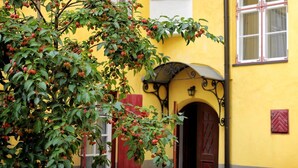 A building with a yellow facade, a red door, and a tree with green leaves and red fruits in front. - Stunning Old Town Getaway with Sauna! (Tallinn)