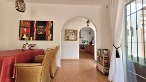 A dining area with a red table, gold chairs, and a wall-mounted painting. An archway leads to a kitchen with a tiled floor and a bookshelf. - Beautiful Casa Jade, 3 Bedroom. Private,secluded pool & gardens. Mountain Views  (AN)