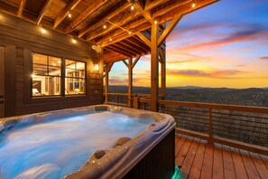 Un jacuzzi en una terraza de madera con vistas a las montañas al atardecer.