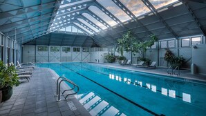 An indoor swimming pool with a glass ceiling, lounge chairs, and potted plants.
