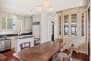 A spacious kitchen with white cabinetry, a wooden dining table, and a built-in glass display cabinet.