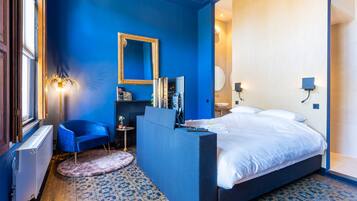 Un dormitorio moderno con una cama grande, un muro azul decorativo, un espejo, una tocador y un pequeño rincón de estar.