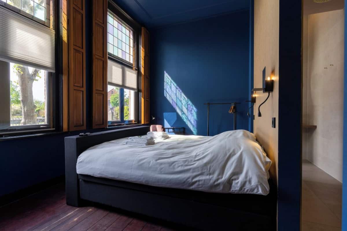 Un dormitorio con una cama grande, una ventana con persianas y una pantalla de proyección en la pared.