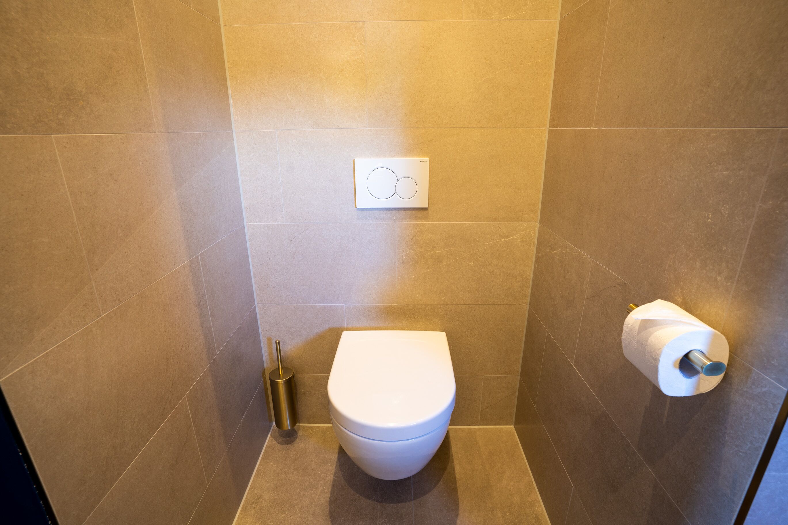 Un baño moderno con inodoro, un botón para tirar de la cadena y un dispensador de papel higiénico.