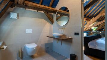 Ein modernes Badezimmer mit Toilette, einem großen, ovalen Spiegel und einer Holzbalkendecke.