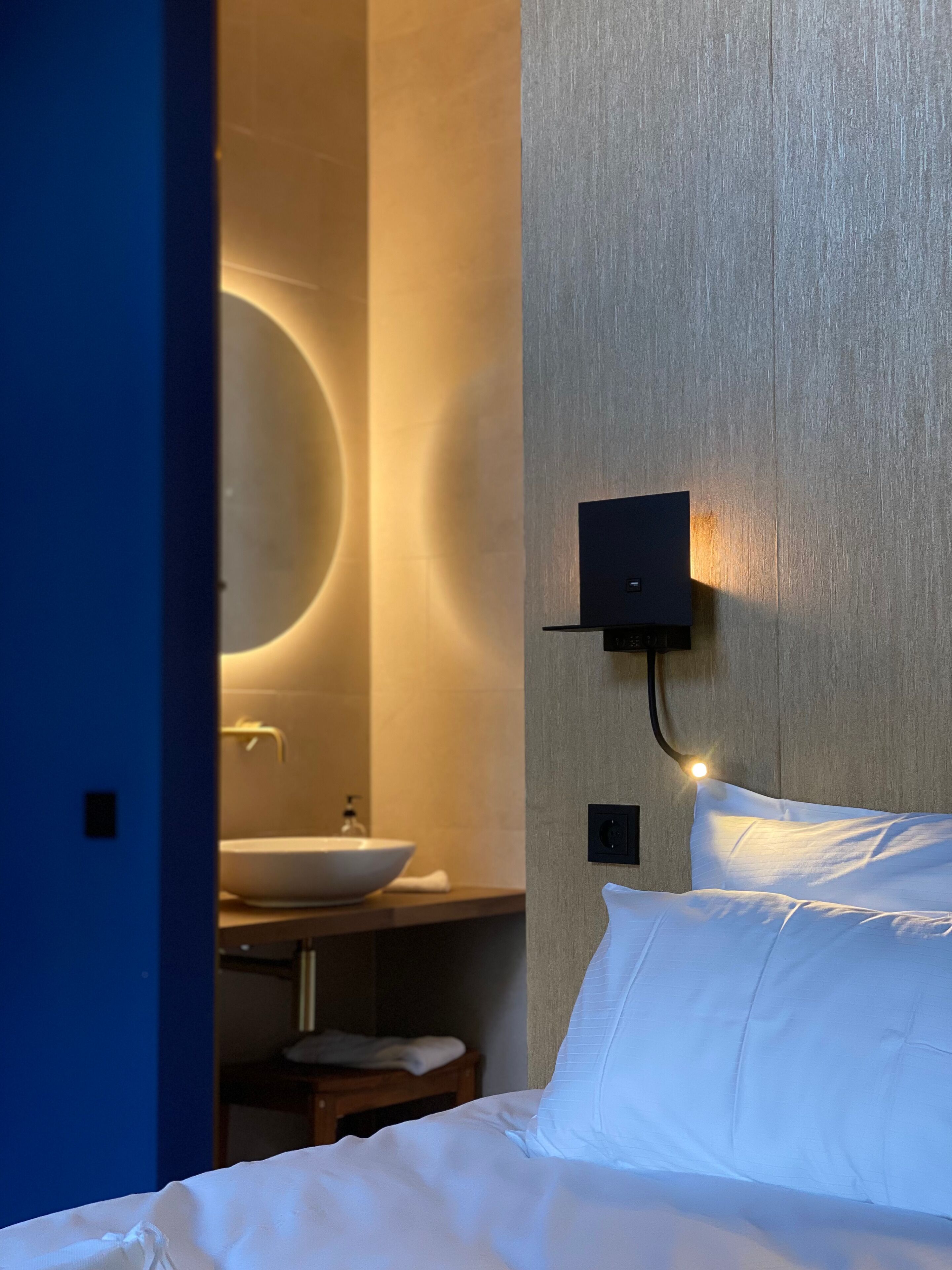A hotel room with a bed, a wall-mounted light, a sink, and a mirror.