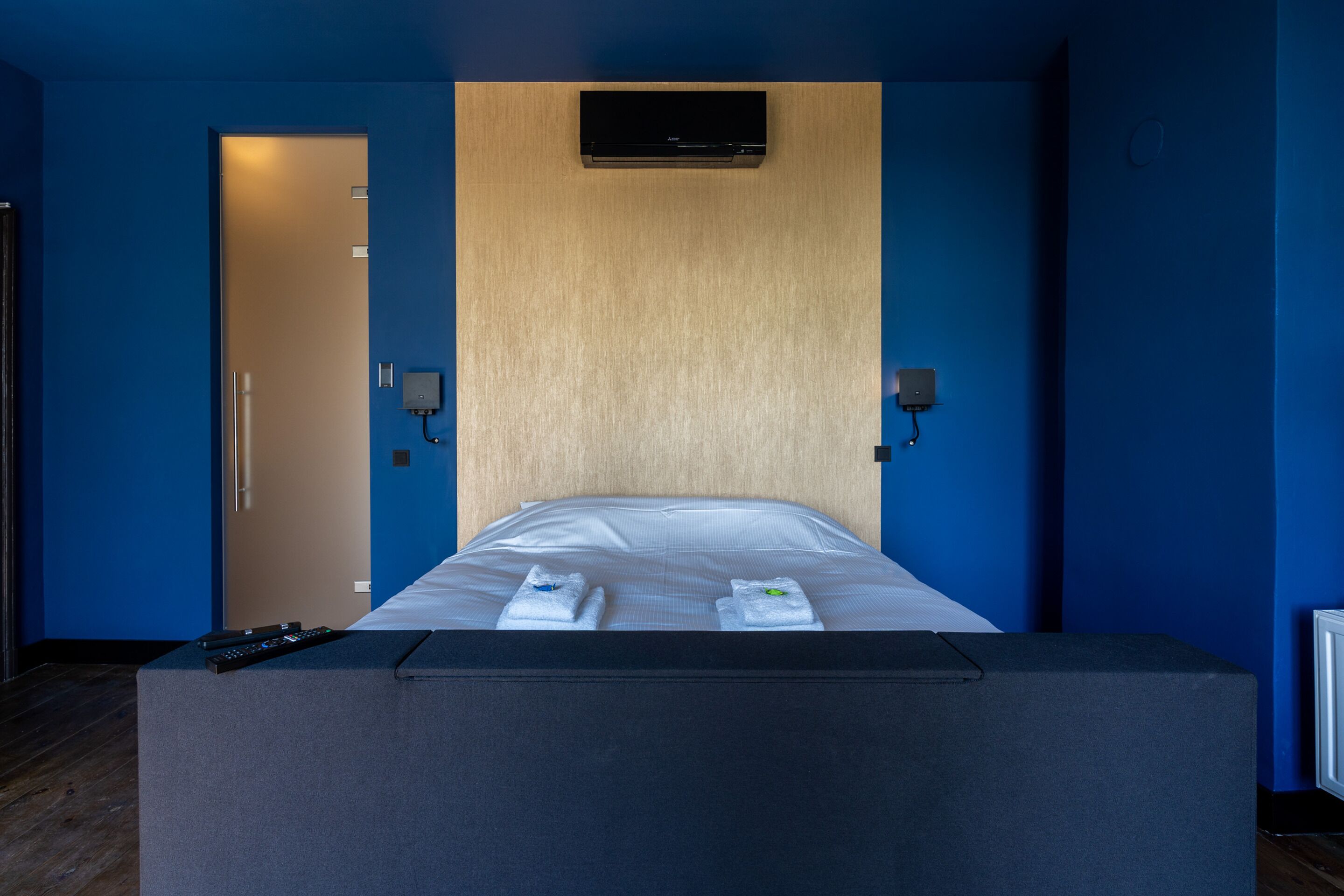 A hotel room with a bed, a control panel, and a remote control on the side table.