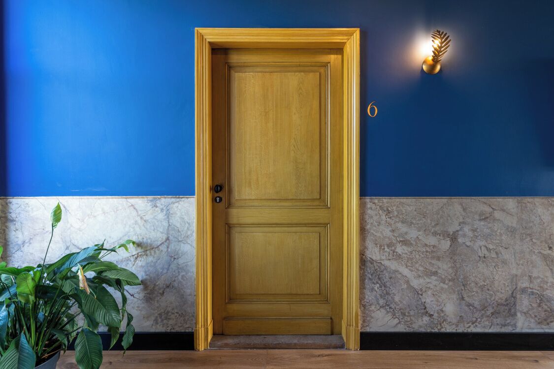 Una puerta de madera con un ojo de cerradura, una pared de mármol y una planta en maceta.