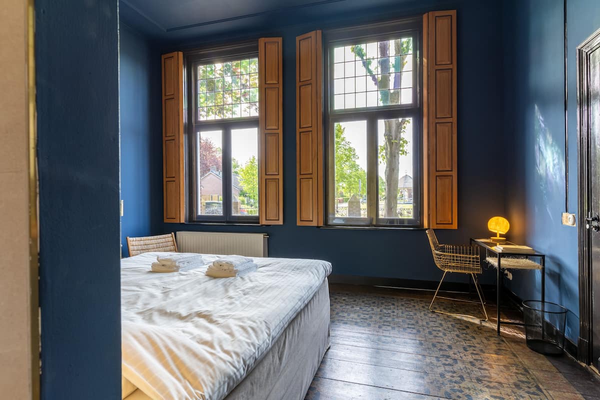 Un dormitorio con cama, una silla, un escritorio y una ventana con contraventanas.
