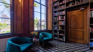 Une bibliothèque avec deux fauteuils de couleur turquoise, une étagère et une grande fenêtre.