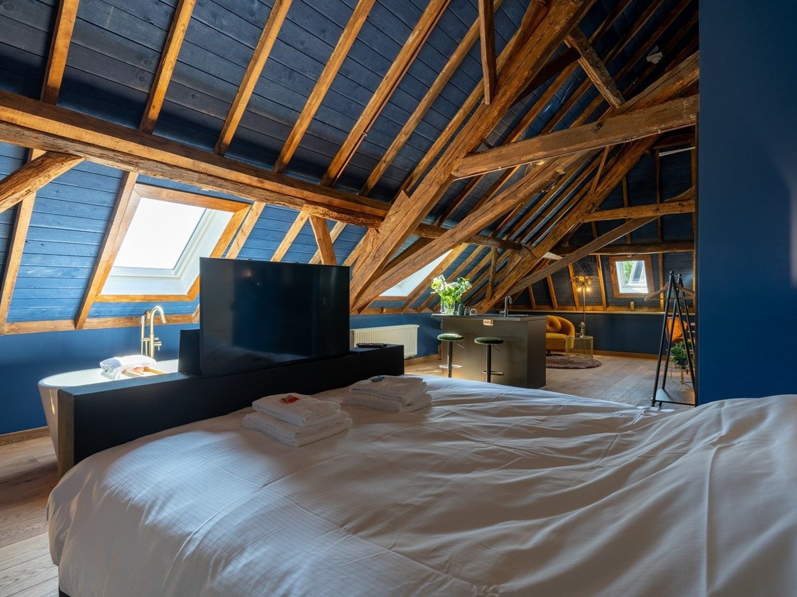A bedroom with a large bed, a TV, a sink, and a small kitchenette.
