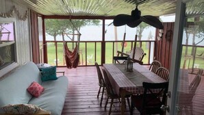 A covered porch with a wooden table and chairs, a sofa with cushions, and a view of the outdoors. - Lakefront Cozy Cottage (Breckenridge)