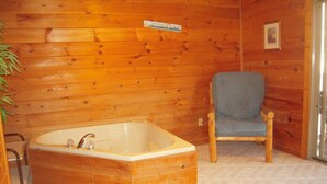 A wooden cabin interior with a wooden bathtub, a blue chair, and a sign on the wall. - Valley View in Shagbark (Sevierville)