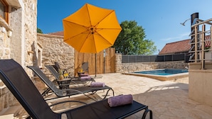 A stone patio with lounge chairs and a yellow umbrella, a swimming pool, and a stone wall. - Villa Izvor Zadarvillas (Skradin)
