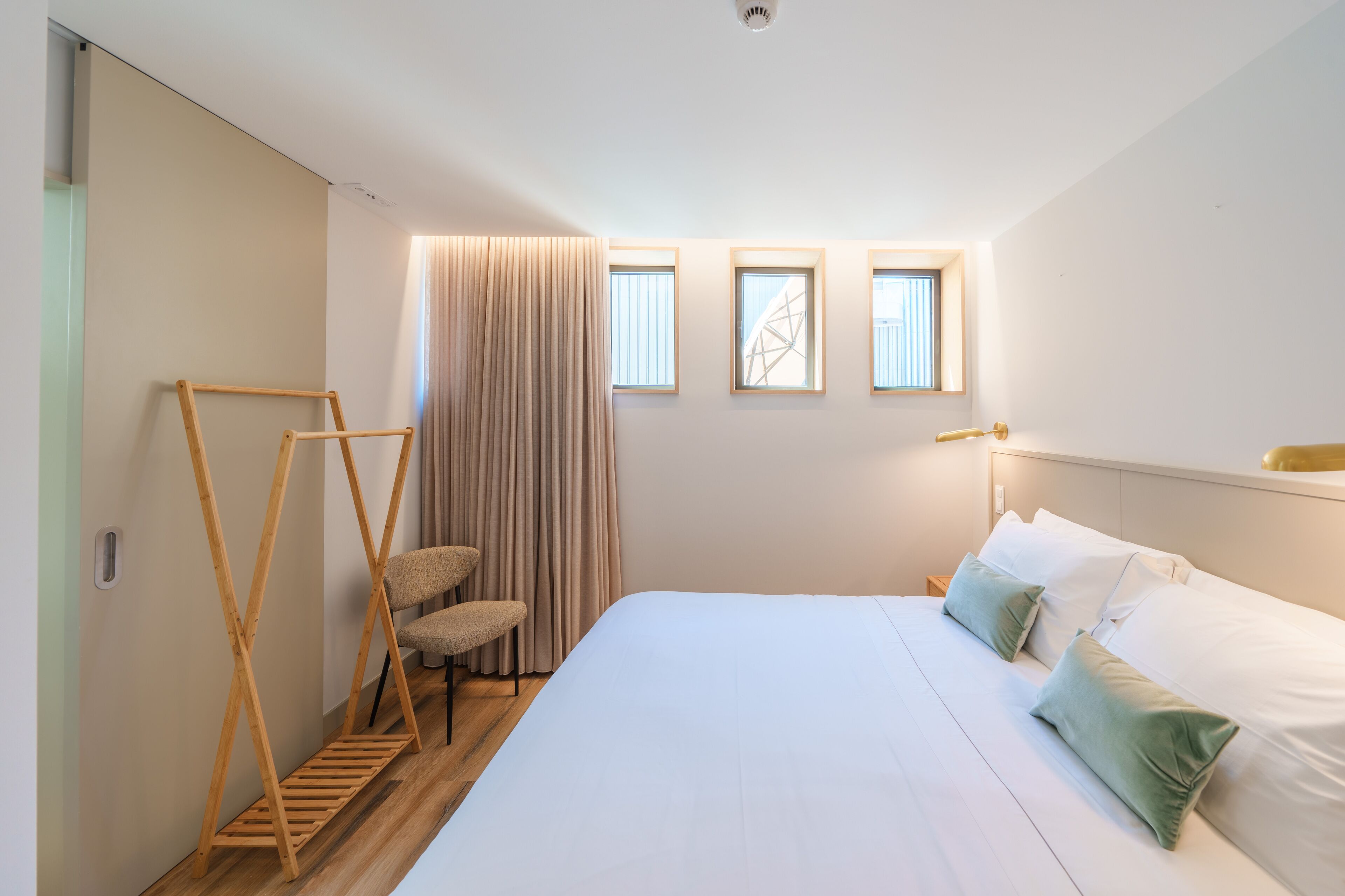 A bedroom with a large bed, a wooden ladder, a chair, and three windows.