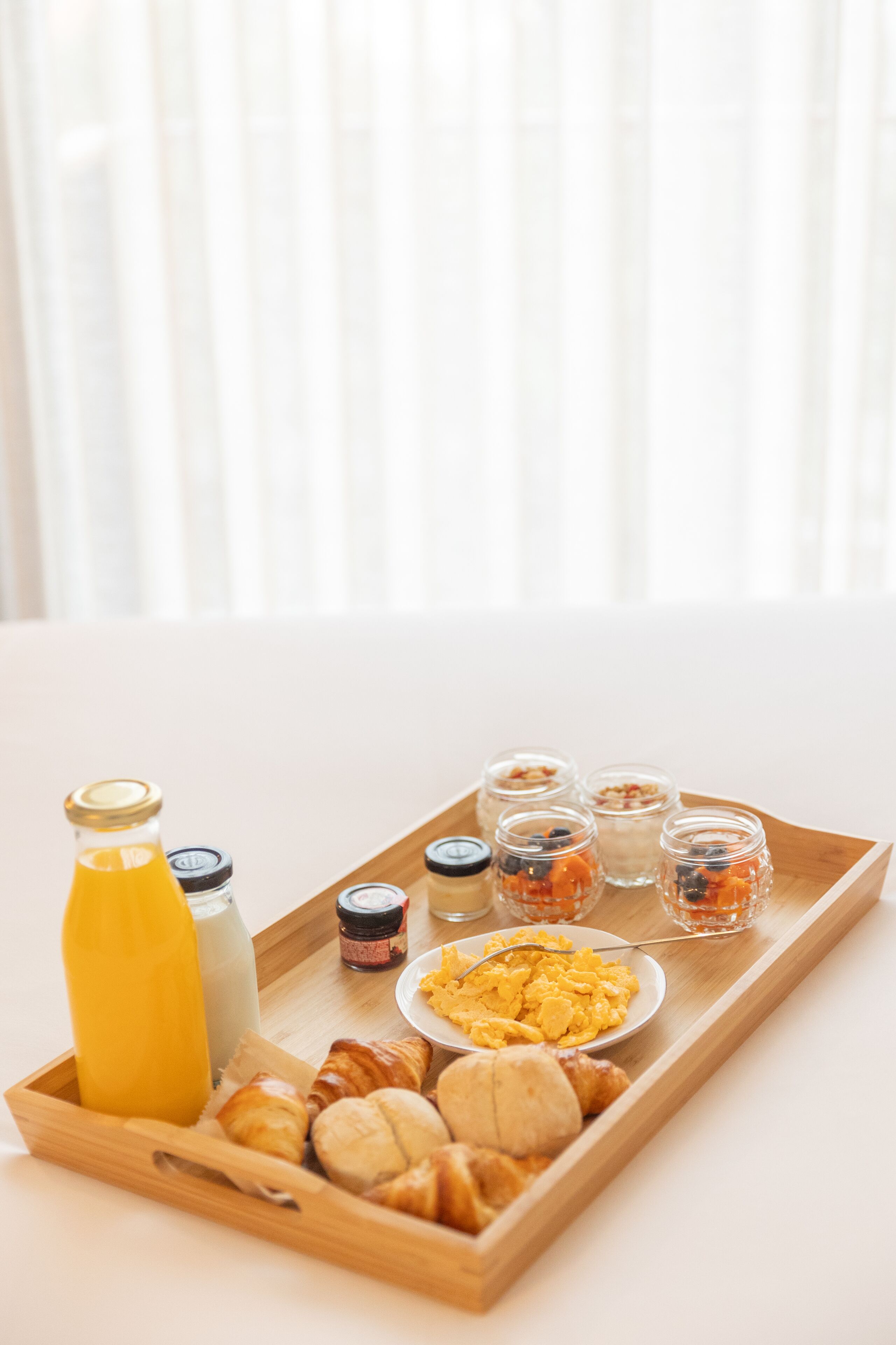 A breakfast tray with croissants, scrambled eggs, and various condiments on a wooden tray.