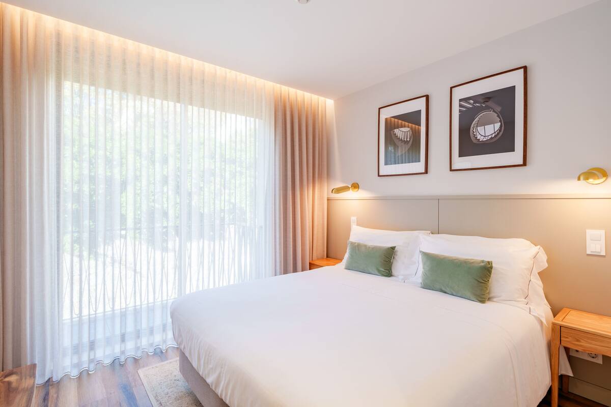 A neatly arranged bedroom with a large bed, a bedside table, and a nightstand. There are two framed pictures on the wall above the bed.