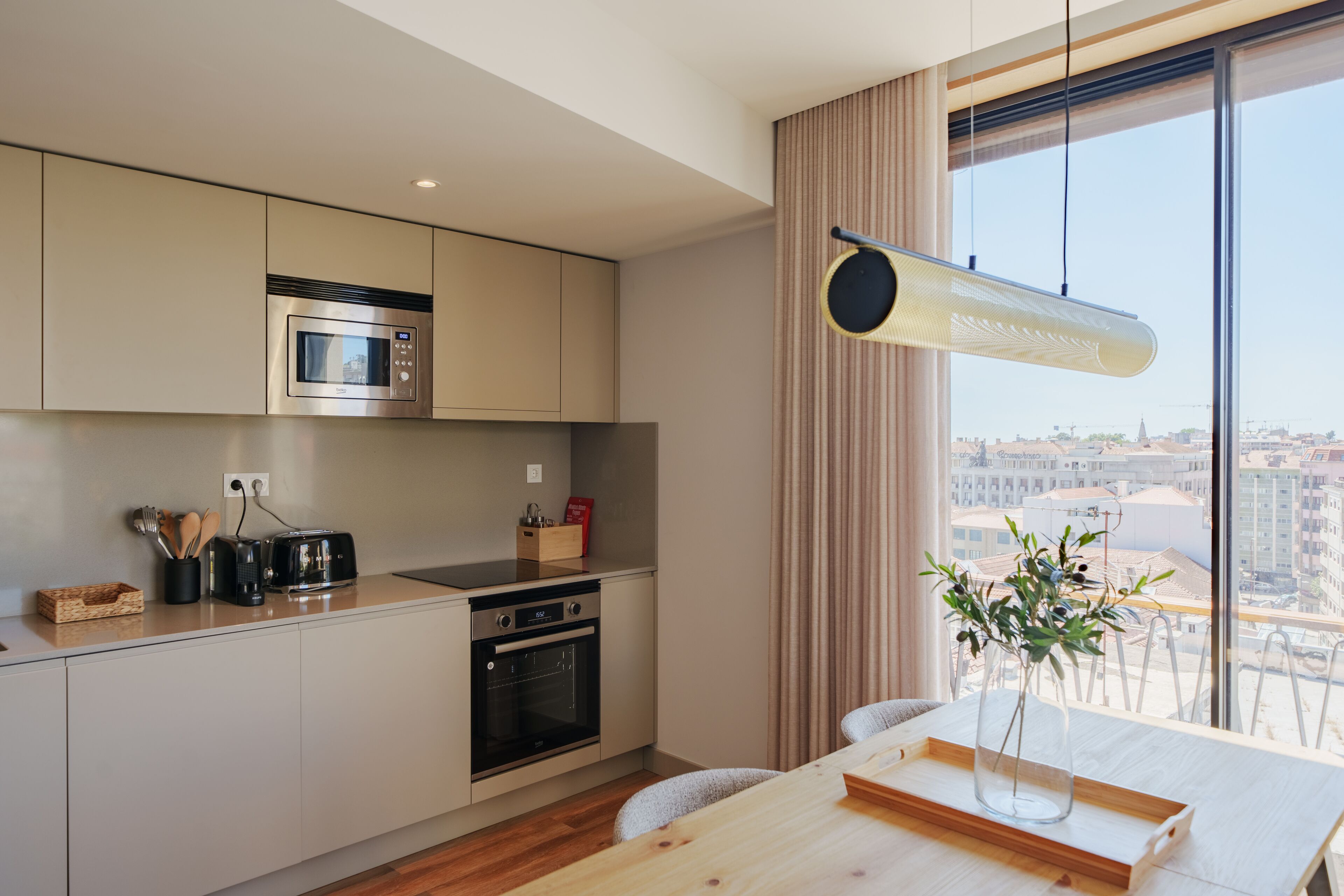 Una cocina moderna con microondas, horno y tostadora integrados. Hay una mesa de comedor con un jarrón de flores y una bandeja de madera.