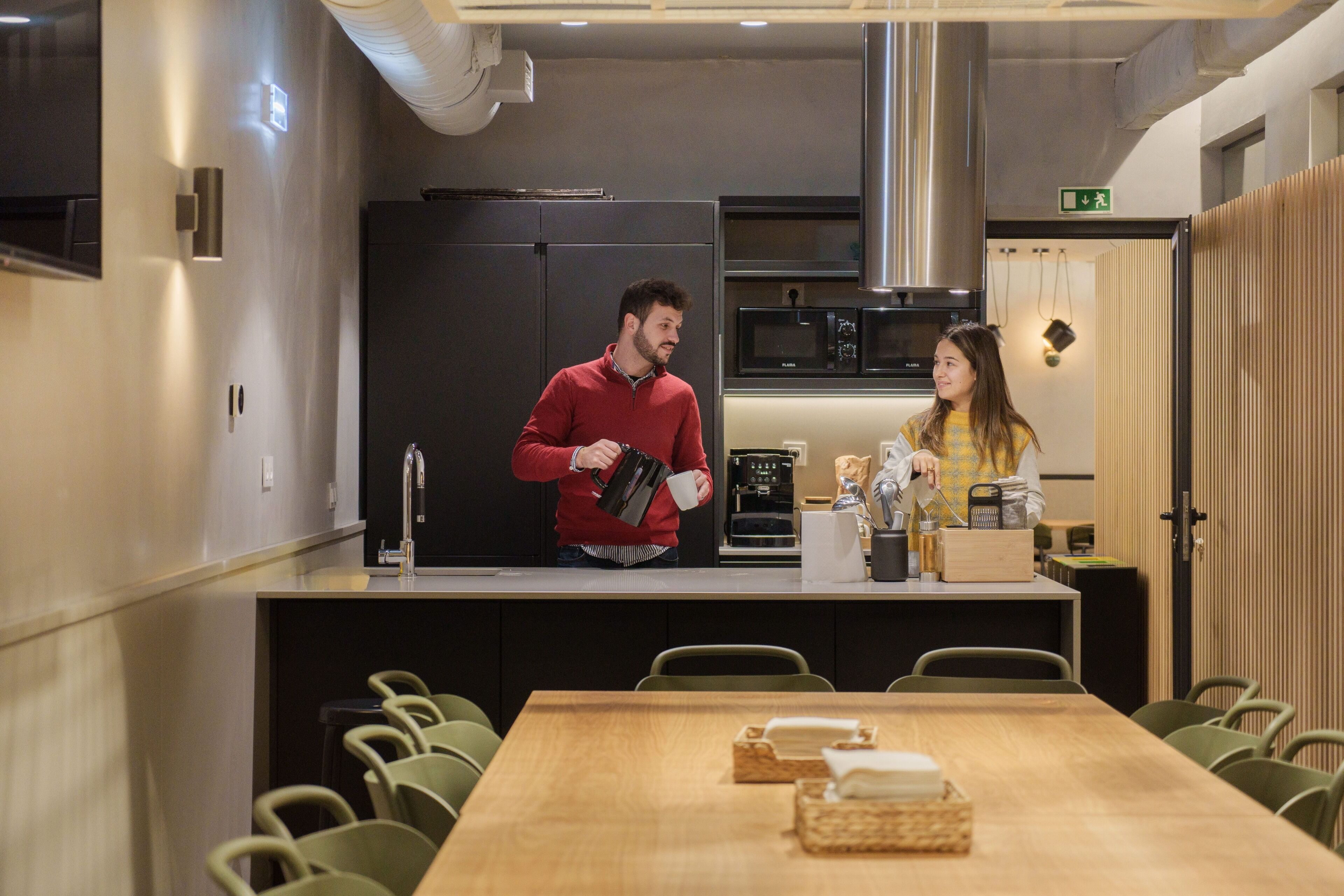 Una cocina moderna con refrigerador, microondas y cafetera. Hay una mesa de comedor de madera con sillas y una pequeña isla de cocina con pileta y encimera.