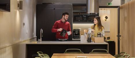 Una cocina moderna con refrigerador, microondas y cafetera. Hay una mesa de comedor de madera con sillas y una pequeña isla de cocina con pileta y encimera.