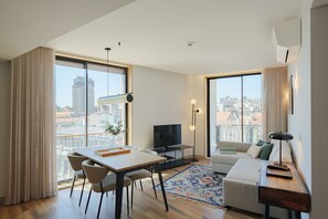 Un soggiorno moderno con zona pranzo, ampie finestre, una televisione a schermo piatto e un divano.
