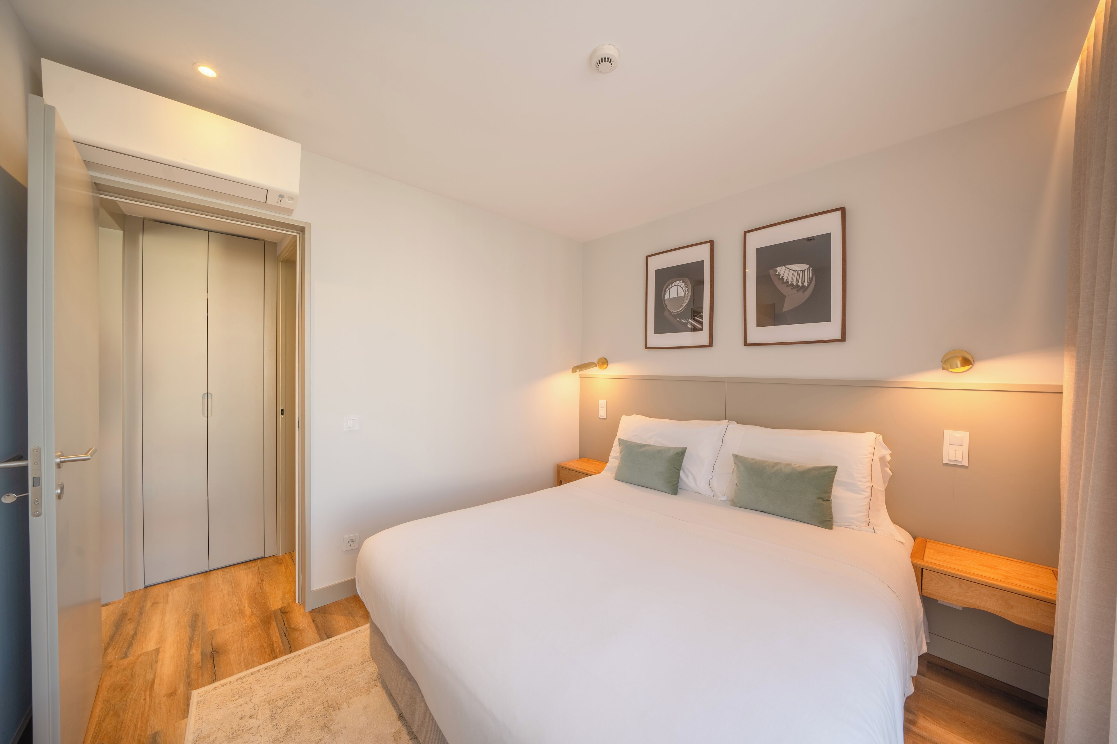 A bedroom with a bed, bedside tables, a wardrobe, and two framed pictures on the wall.