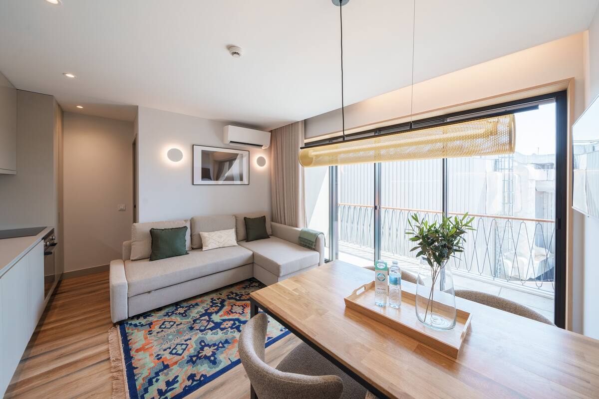 A modern living room with a sofa, a dining table, and a large window with a view.