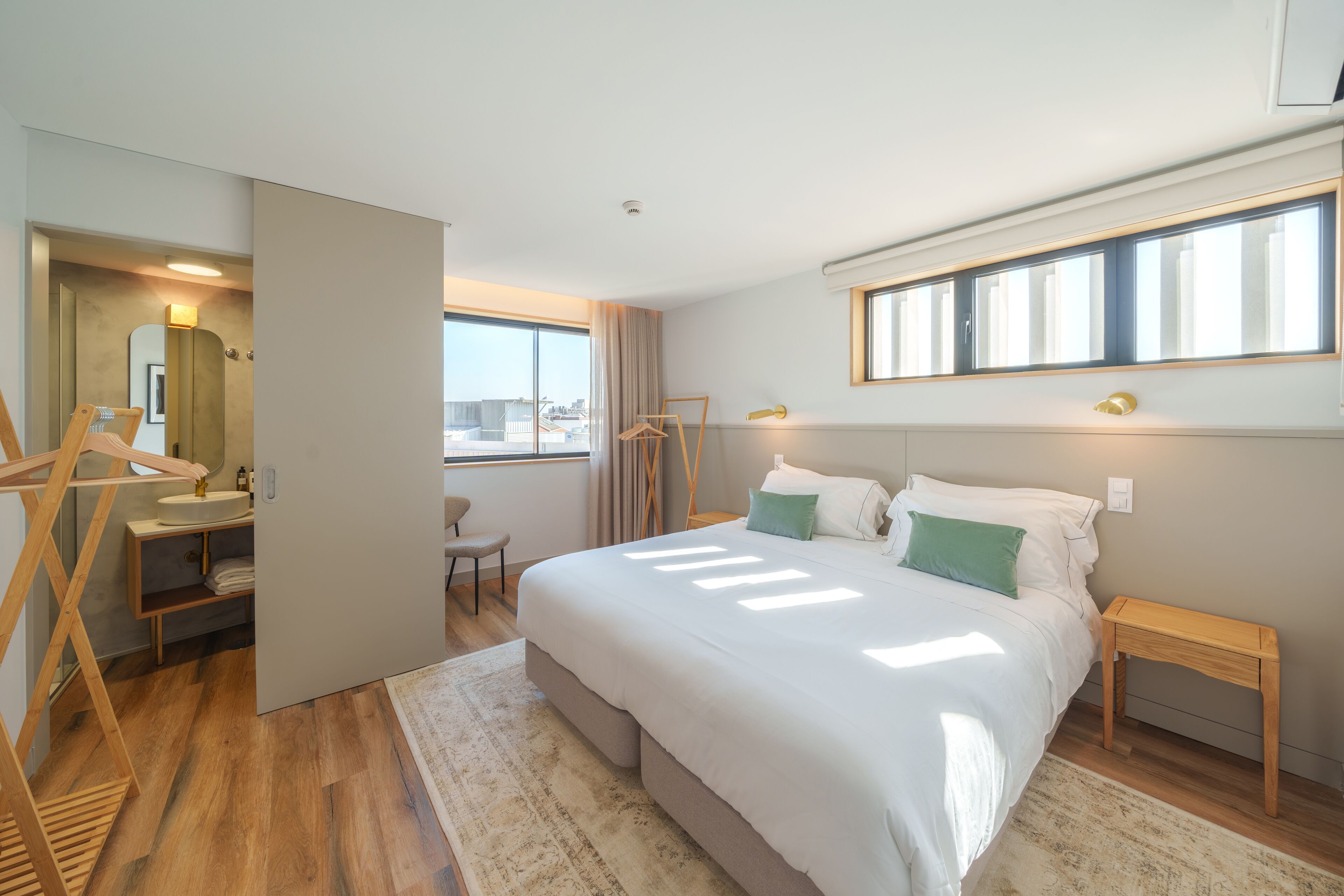 Ein modernes Hotelzimmer mit einem großen Bett, einem Schreibtisch mit Stuhl, einem Schminktisch mit Spiegel und einem Fenster mit Vorhängen.