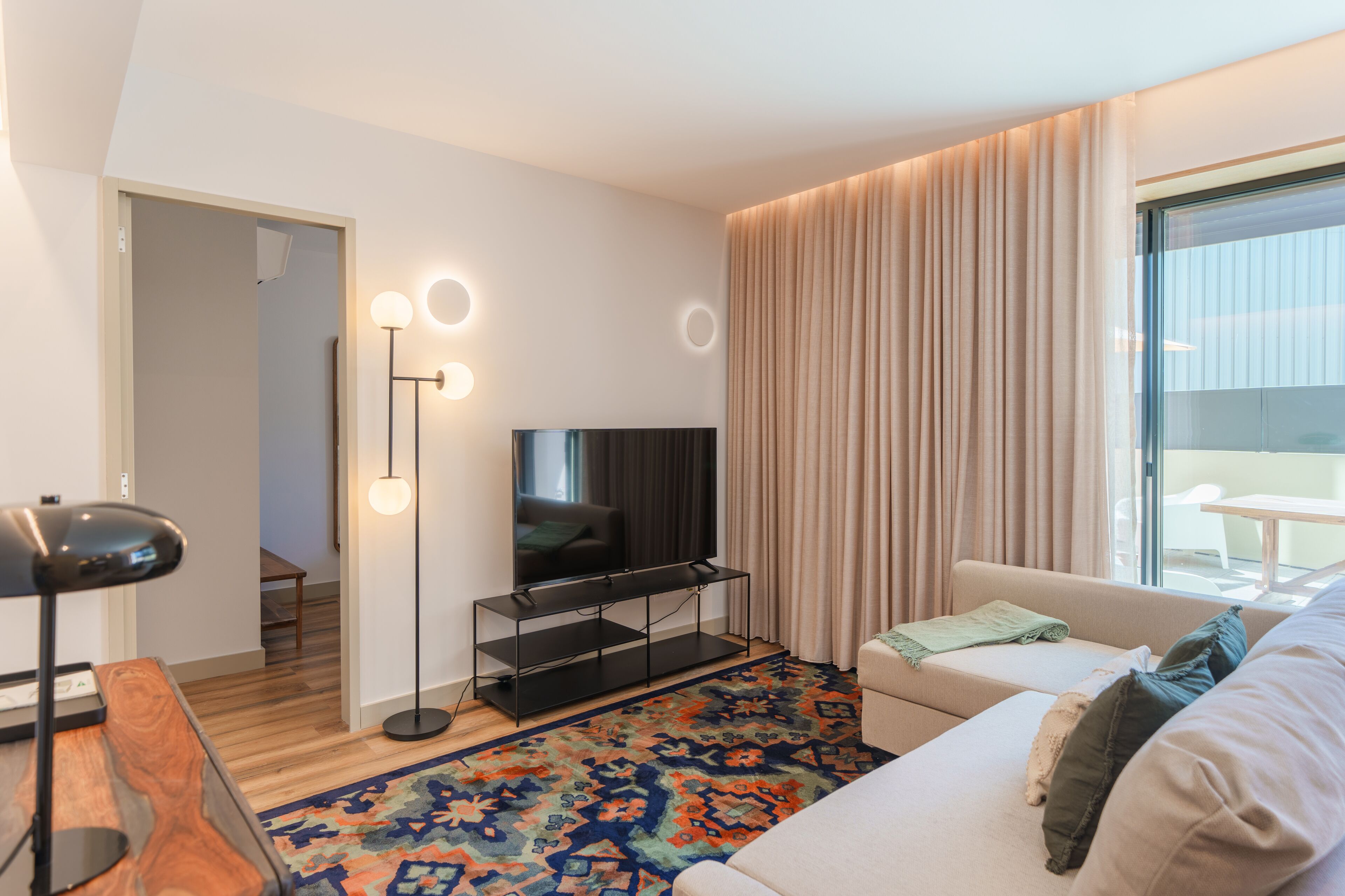 A modern living room with a flat-screen TV, a sofa, a coffee table, a floor lamp, and a patterned rug.