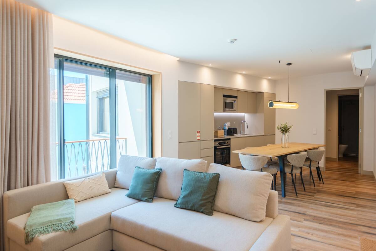 A modern living room with a sofa, a dining table, and a kitchen area.