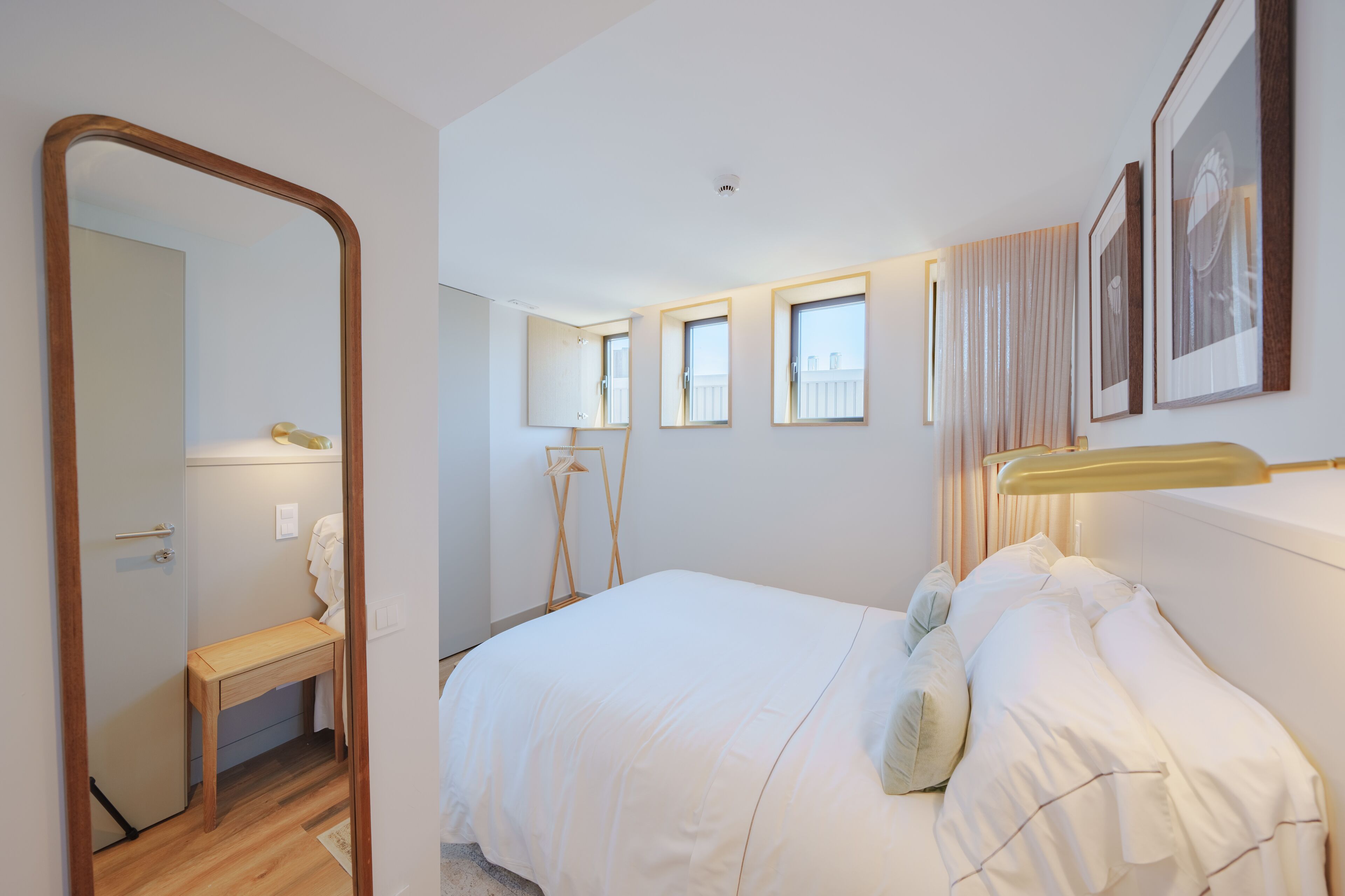 A bedroom with a bed, a bedside table, a mirror, and a window.