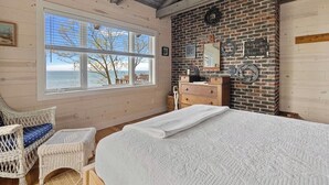 A bedroom with a large window, a bed, a dresser, and a brick wall.