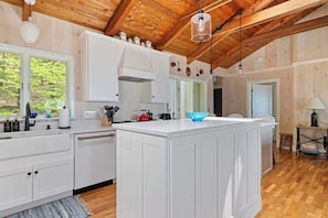 A kitchen with white cabinets, a wooden ceiling, and a large island with a blue bowl. - Juniper Presents: Majestic Beachfront Beauty on the Sunset Coast (Bridgman)