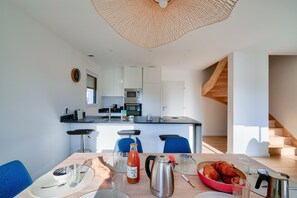 A modern kitchen with a central island, bar stools, and a dining table set with plates, glasses, and a bottle. - Nice house for 8 - 950m from the beach & harbour (Penmarch)