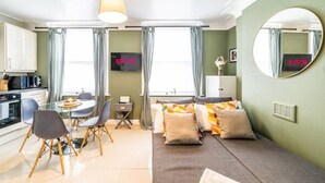 A modern living room with a sofa, a dining table with chairs, a TV, and a kitchen area with a microwave and kettle. - [Covent Garden-Fitzrovia]Central London Apartment (London)