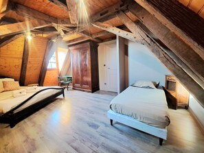An attic bedroom with wooden beams, a bed, a chair, and a wardrobe. - Maison Périgourdine Restaurée (Beaumontois-en-Périgord)