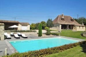 A pool area with lounge chairs and a house in the background. - Maison Périgourdine Restaurée (Beaumontois-en-Périgord)