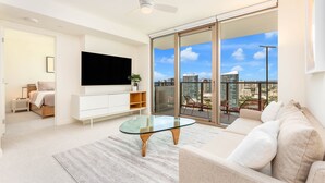 A modern living room with a flat-screen TV, a glass coffee table, a sofa, and a balcony with a city view.