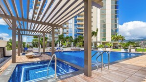 A rooftop pool area with a wooden deck, lounge chairs, and a view of high-rise buildings.