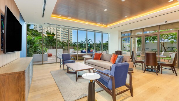 A modern hotel lobby with a sofa, chairs, a TV, and a view of the outdoors.