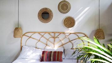 Una cama con un cabecero tejido, dos tapices tejidos en la pared y una lámpara colgante de tejido.
