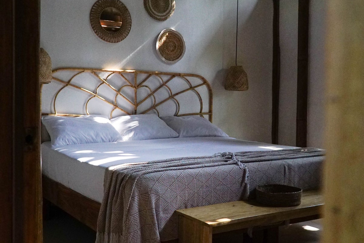 Een kamer met een bed, een houten bank en wanddecoraties van geweven materiaal.