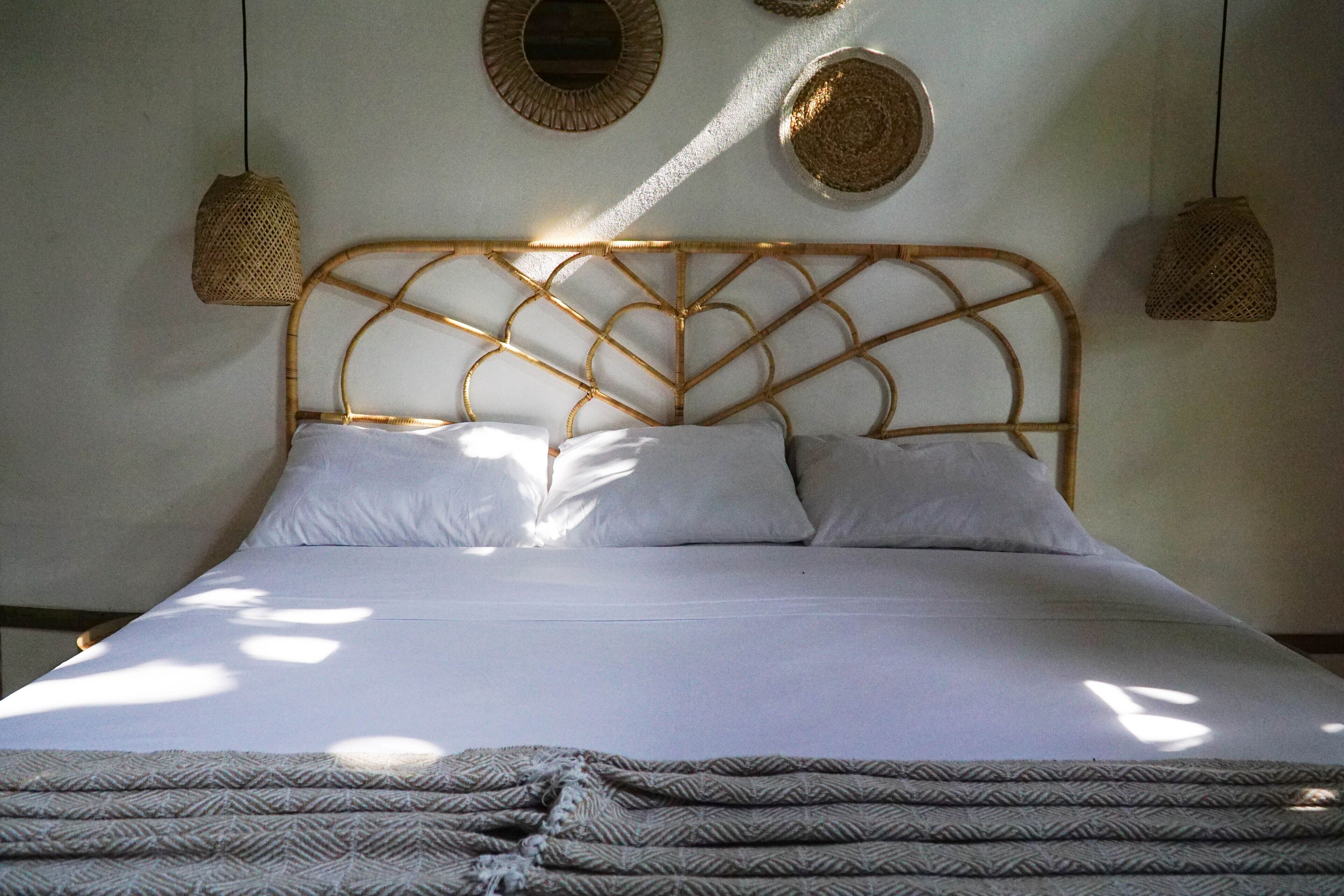 A bed with a woven headboard, white bedding, and a patterned throw blanket.