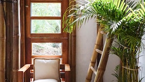 Une chaise en bois avec un coussin, dans une pièce décorée d’éléments en bambou et agrémentée d’une grande plante en pot.