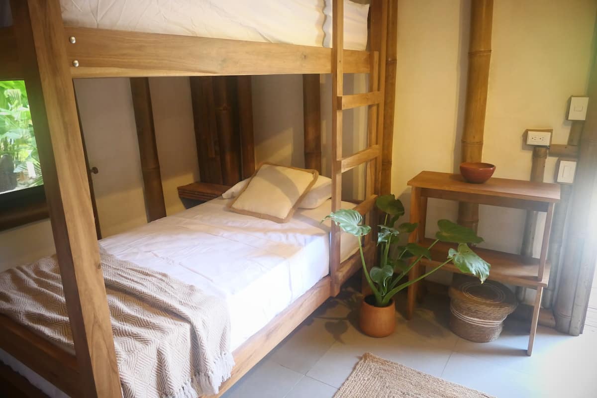 Een stapelbed met houten frame, een nachtkastje met een kom, en een bloempot.