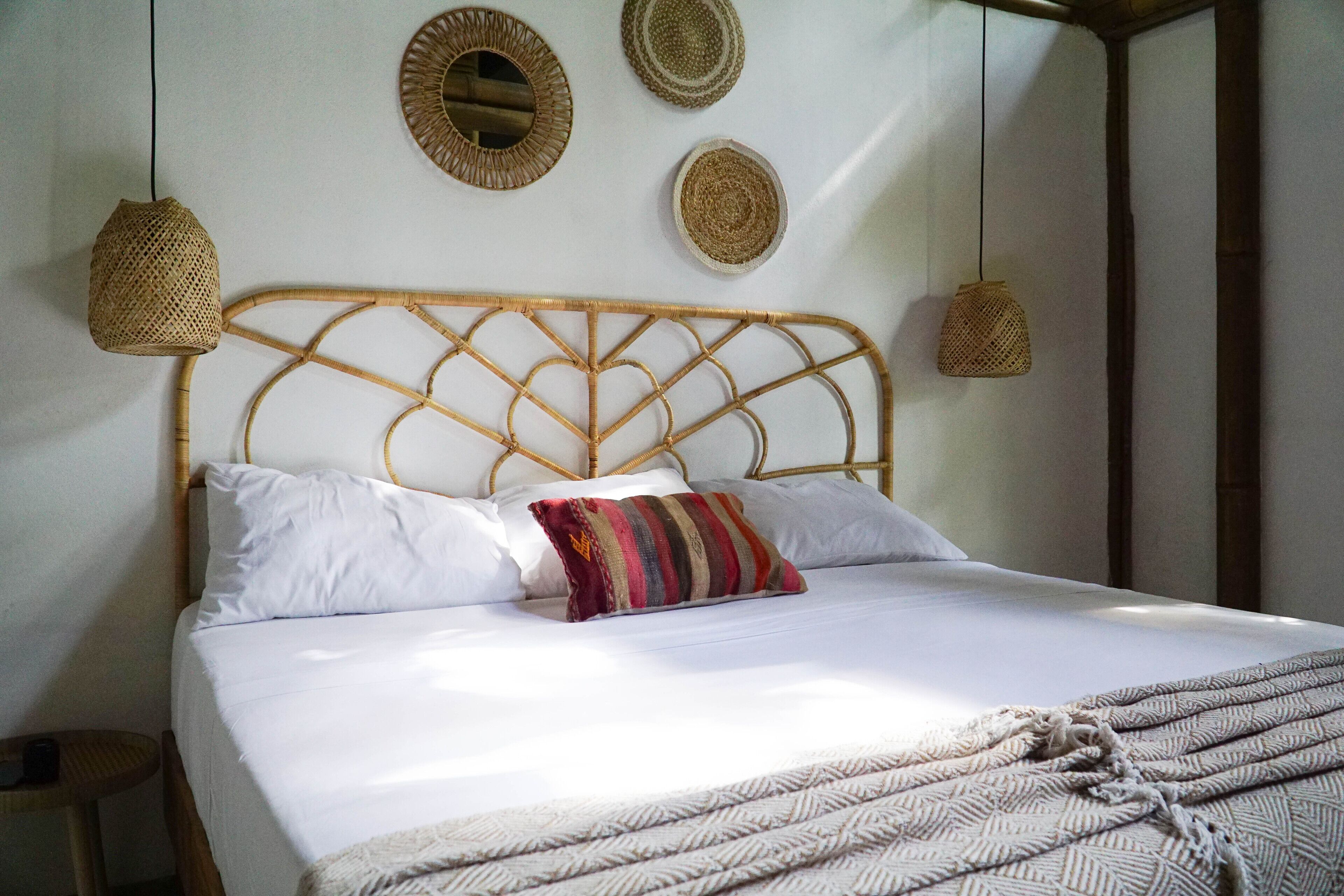 Una cama bien hecha con sábanas blancas y un cojín a rayas, un cabecero tejido y tres tapices de pared tejidos.