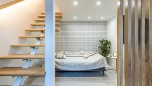 A bedroom with a bed, a wooden staircase, and a geometric-patterned wall. - Lovely Apartment by National Museum (Budapest)