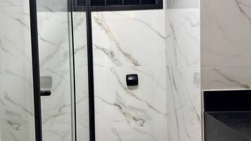 Et badeværelse med en glasafskærmet brusekabine, et hvidt toilet og en sort vask.